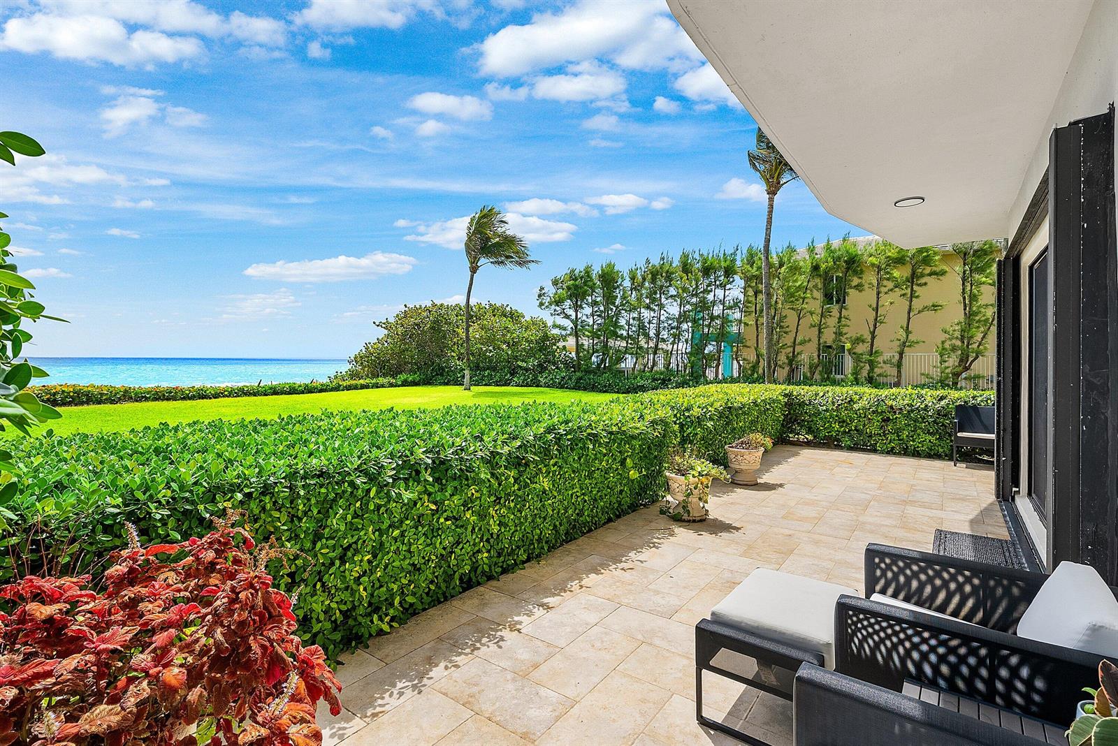 A patio with outdoor furniture overlooks a manicured lawn, a hedge, and the ocean — 3951 N Ocean Boulevard # 101, Gulf Stream FL 33483, GULF STREAM, FL