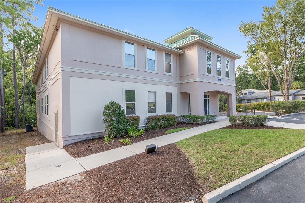 A two-story commercial building with light-colored stucco walls and a green metal roof — 1014 NW 57TH STREET, GAINESVILLE, FL