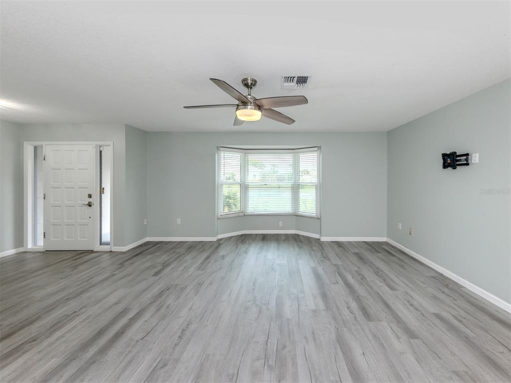 A living room with light gray walls, wood-look flooring, a ceiling fan, and a bay window — 1053 DERIAN PLACE, NOKOMIS, FL