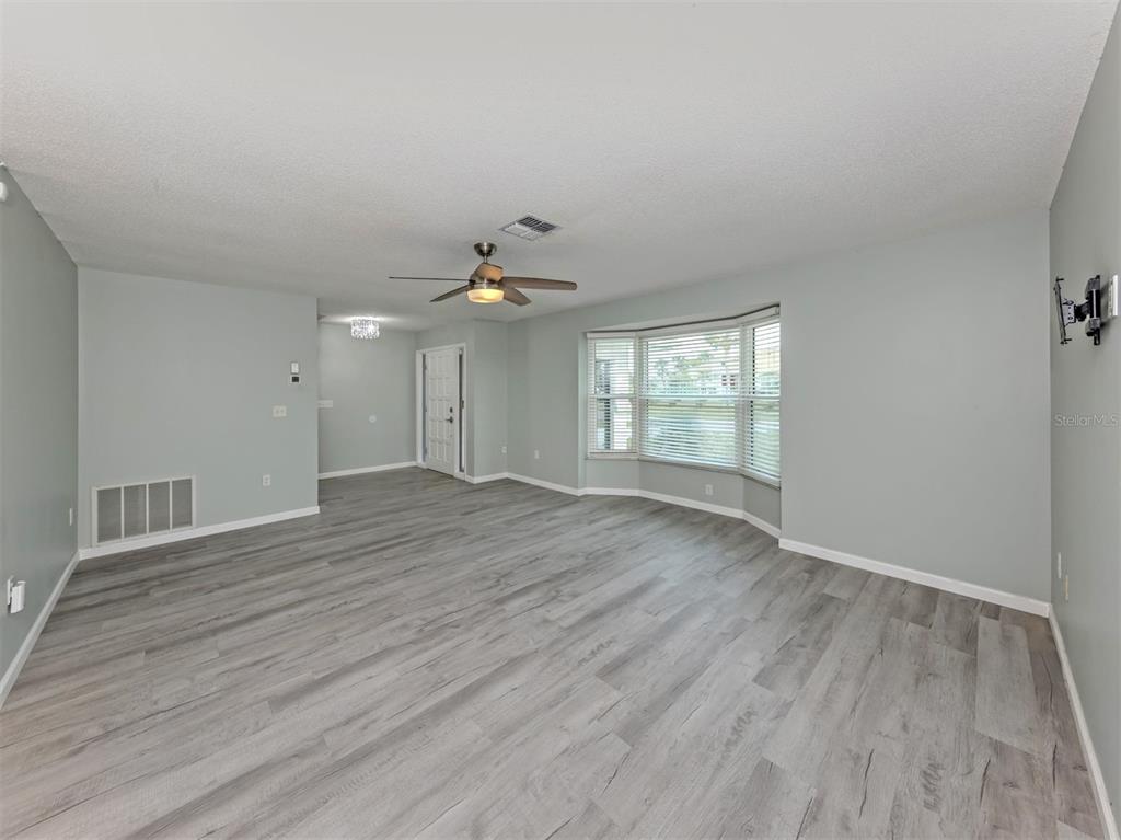 A spacious living room features light gray walls, wood-look flooring, a ceiling fan, and bay windows — 1053 DERIAN PLACE, NOKOMIS, FL
