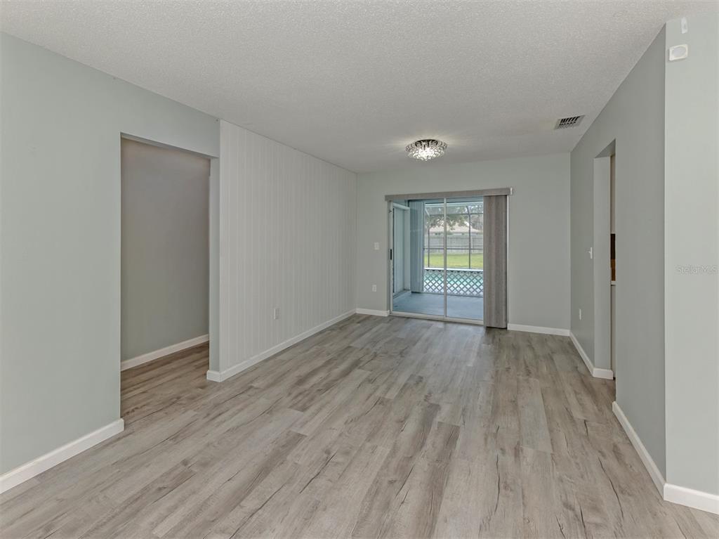 An empty living room features light gray walls, wood-look flooring, and a sliding glass door — 1053 DERIAN PLACE, NOKOMIS, FL