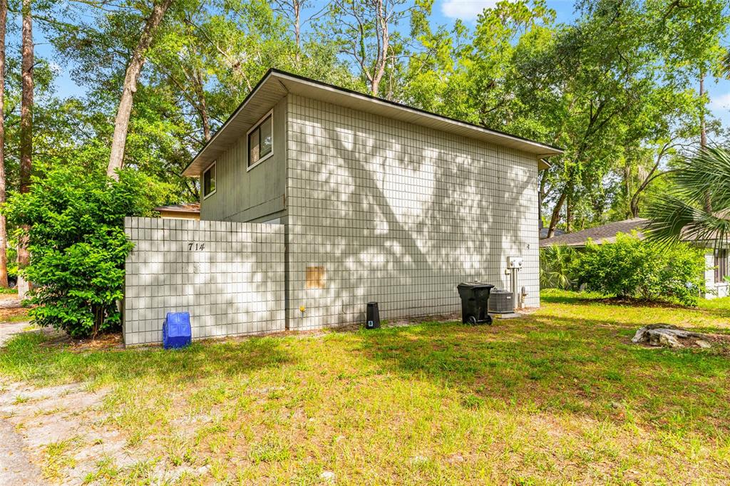 A two-story building with light-colored block siding stands in a grassy, tree-filled yard — 714 SW 69TH STREET, GAINESVILLE, FL