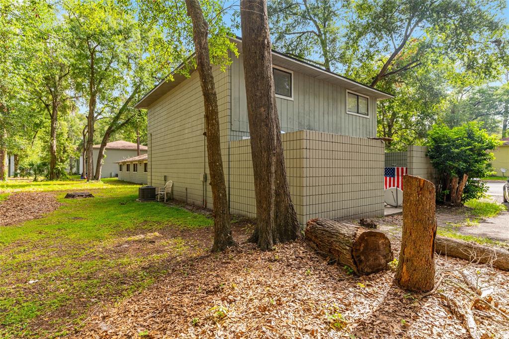 A two-story house with gray siding and a concrete block wall stands among trees — 714 SW 69TH STREET, GAINESVILLE, FL