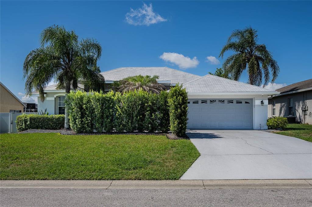 A single-story house with a white garage, a green hedge, and two palm trees — 6077 CASON WAY, LAKELAND, FL