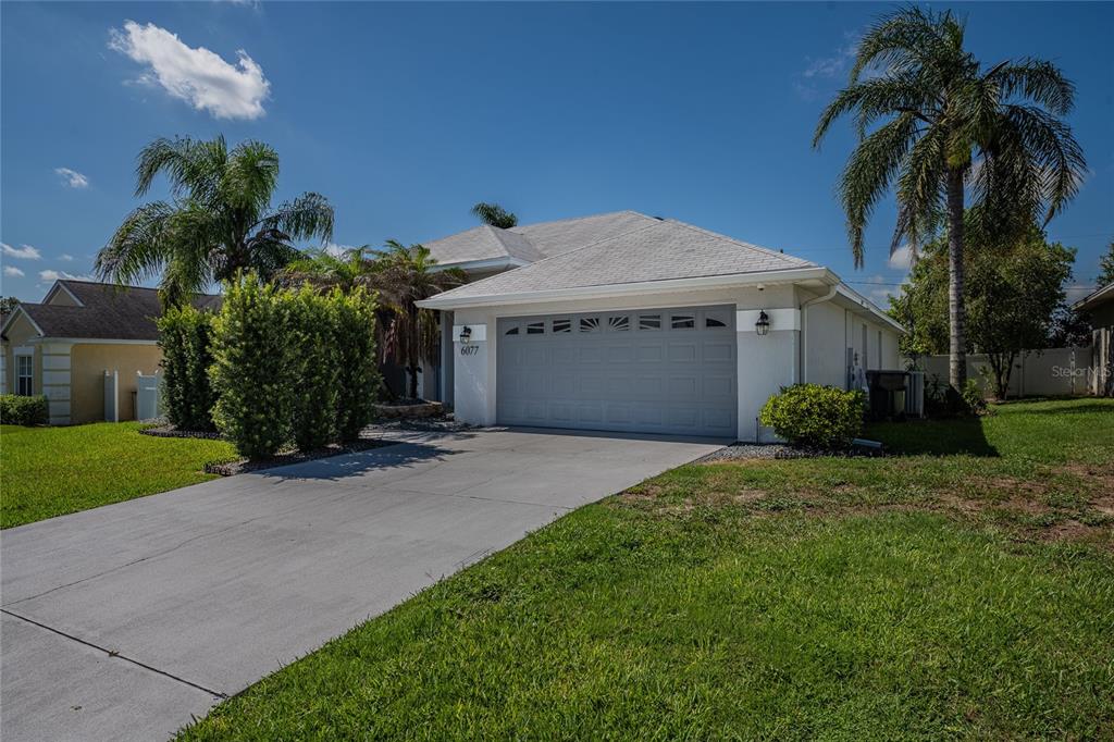 A single-story house with a gray garage door, a concrete driveway, and palm trees — 6077 CASON WAY, LAKELAND, FL
