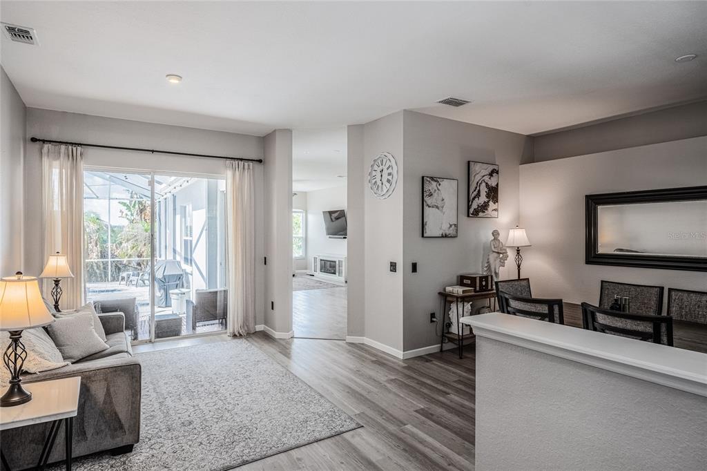 A living room with gray flooring, a sliding glass door, and an adjacent dining area — 6077 CASON WAY, LAKELAND, FL