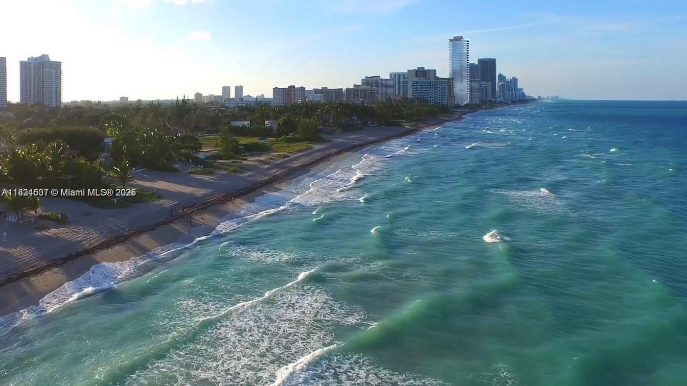 An aerial view shows a sandy beach along the ocean with high-rise buildings in the background — 3180 S Ocean Dr # 1602, Hallandale Beach FL 33009, HALLANDALE BEACH, FL