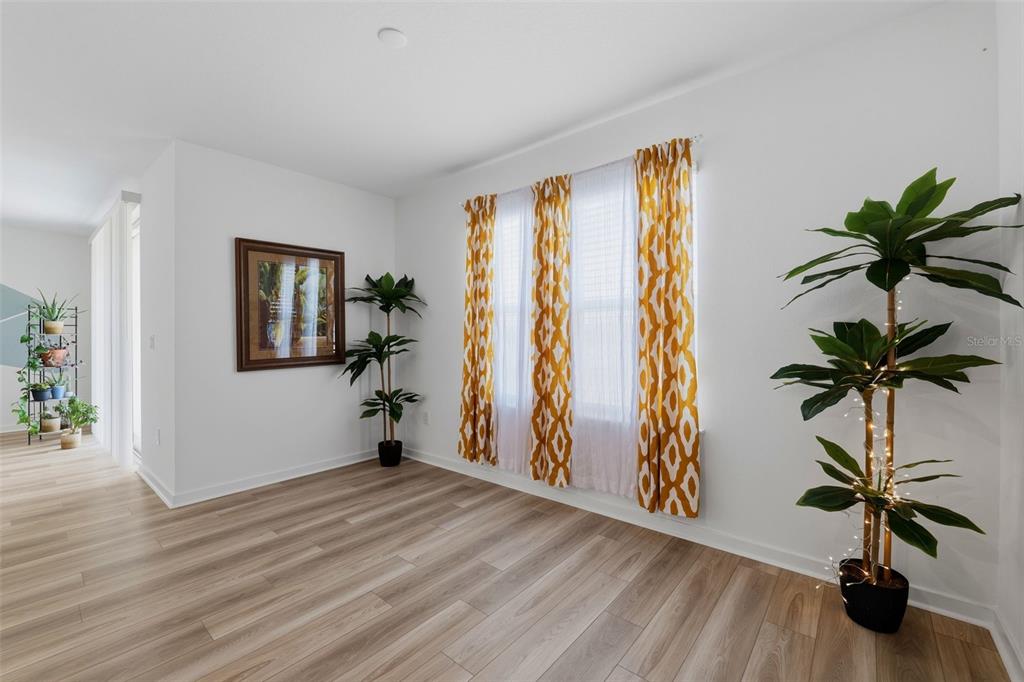 A bright room features light wood-look flooring, white walls, yellow patterned curtains, and potted plants — 10517 HIDDEN BANKS GLEN, PARRISH, FL