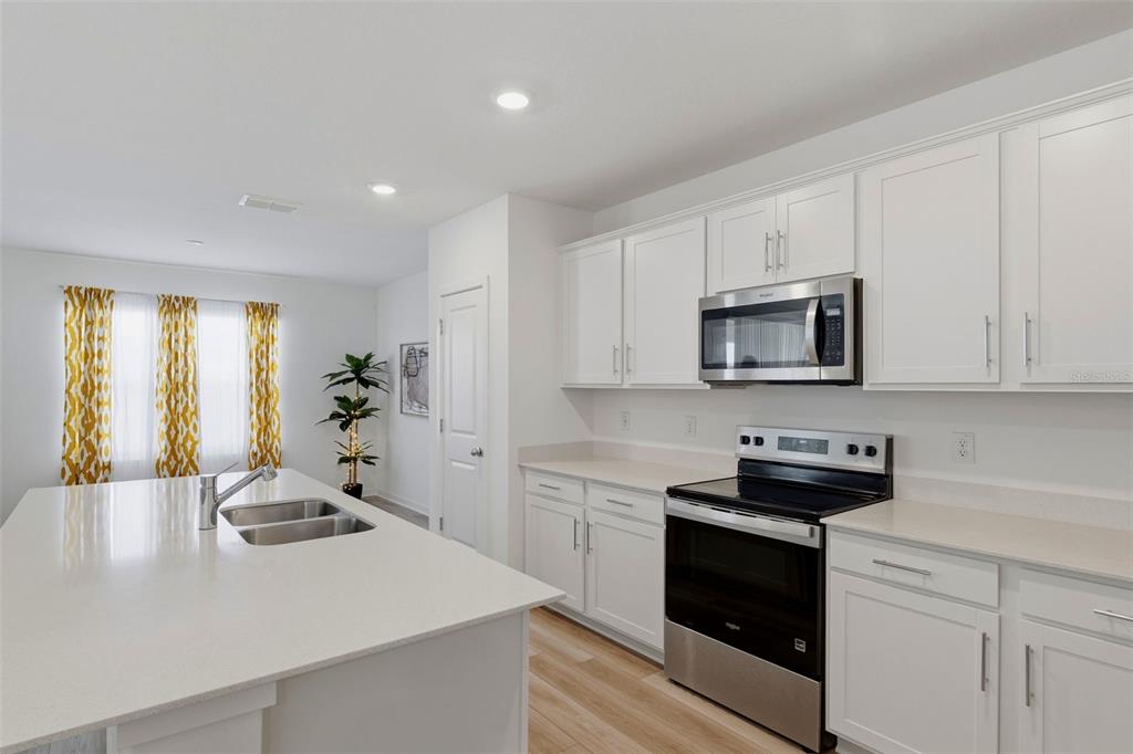 A modern kitchen features white cabinets, stainless steel appliances, and a large central island — 10517 HIDDEN BANKS GLEN, PARRISH, FL