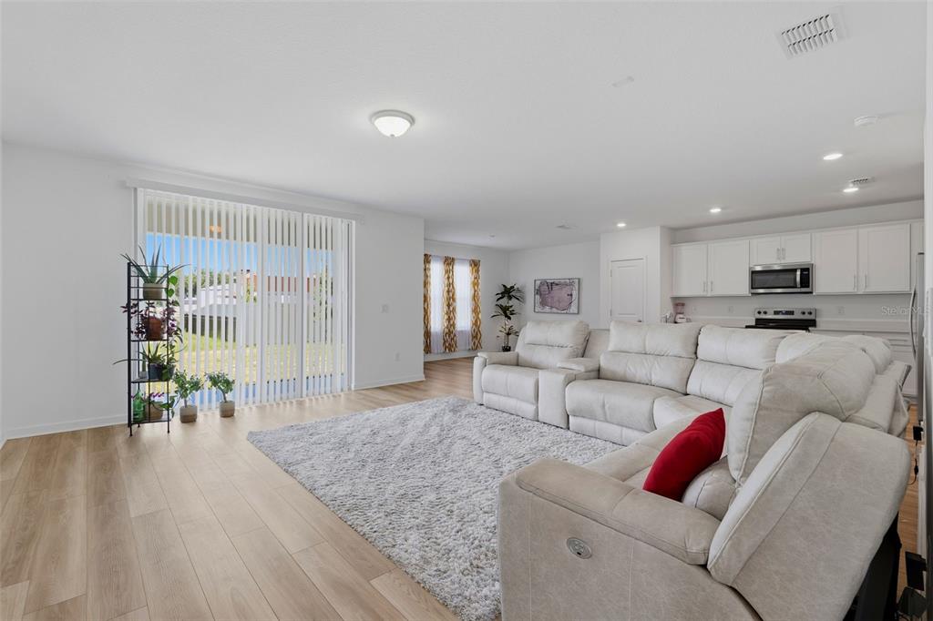 A spacious living room features light wood-look flooring, a large sectional sofa, and sliding glass doors — 10517 HIDDEN BANKS GLEN, PARRISH, FL