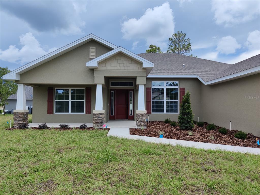 A single-story house with a tan stucco exterior, stone-based columns, and a red front door — 1 CHRYSANTHEMUM COURT, HOMOSASSA, FL