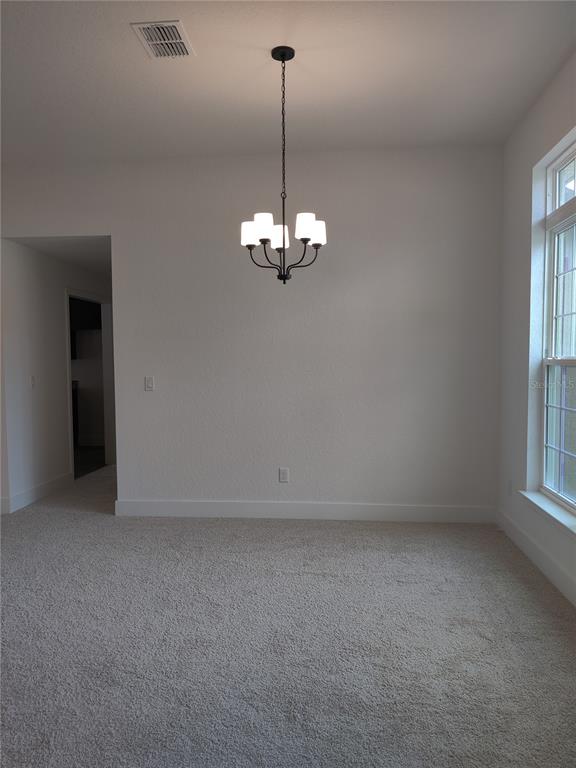 A dining area features beige carpeting, white walls, and a black four-light chandelier — 1 CHRYSANTHEMUM COURT, HOMOSASSA, FL