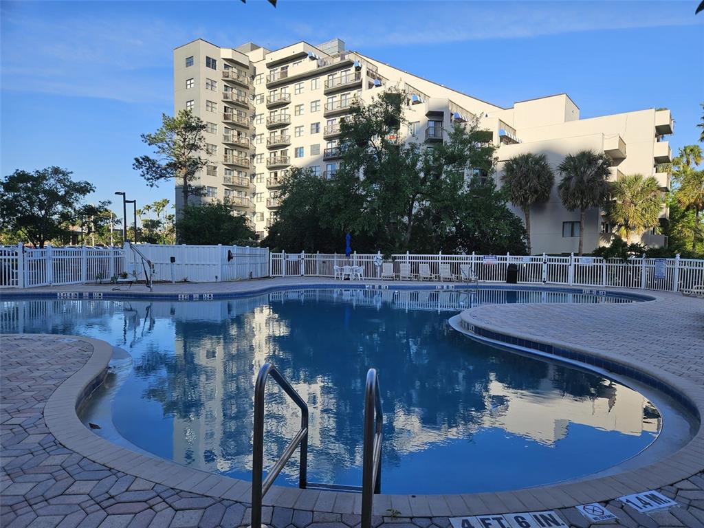 A swimming pool with a metal ladder sits in front of a multi-story apartment building — 6165 CARRIER DRIVE UNIT 3201, ORLANDO, FL