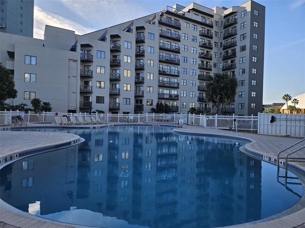A multi-story apartment building stands behind a curved swimming pool with a white fence — 6165 CARRIER DRIVE UNIT 3201, ORLANDO, FL