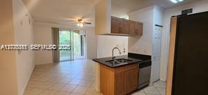 A kitchen with wood cabinets and a black countertop opens to a tiled living area — 6386 Emerald Dunes Dr, West Palm Beach FL 33411, WEST PALM BEACH, FL