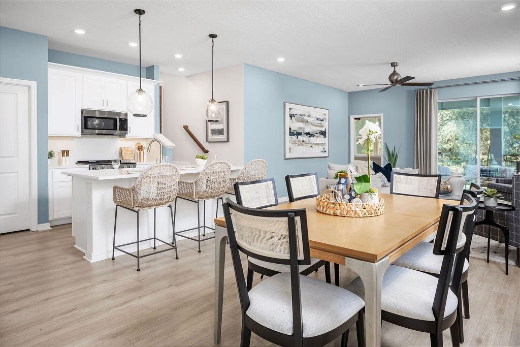 A bright open-concept kitchen and dining area featuring white cabinetry, light wood flooring, and pendant lighting — 5200 LUISA COURT, ST CLOUD, FL
