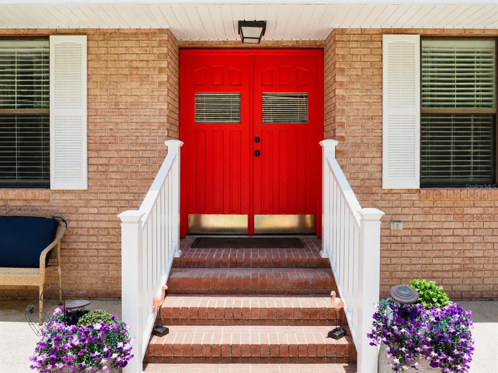 A brick house exterior features a bright red double front door with white railings — 12820 NW 116TH PLACE, ALACHUA, FL