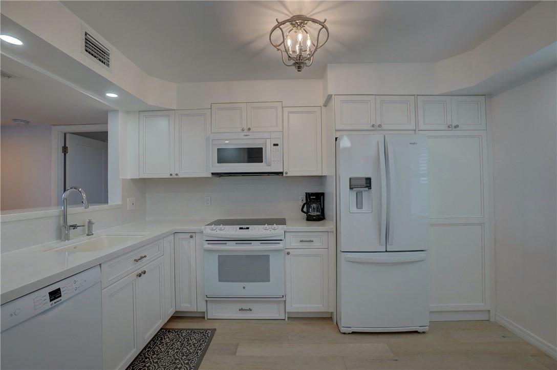 A white kitchen features white cabinetry, white appliances, a light countertop, and light wood flooring — 2871 N Ocean Boulevard # C519, Boca Raton FL 33431, BOCA RATON, FL