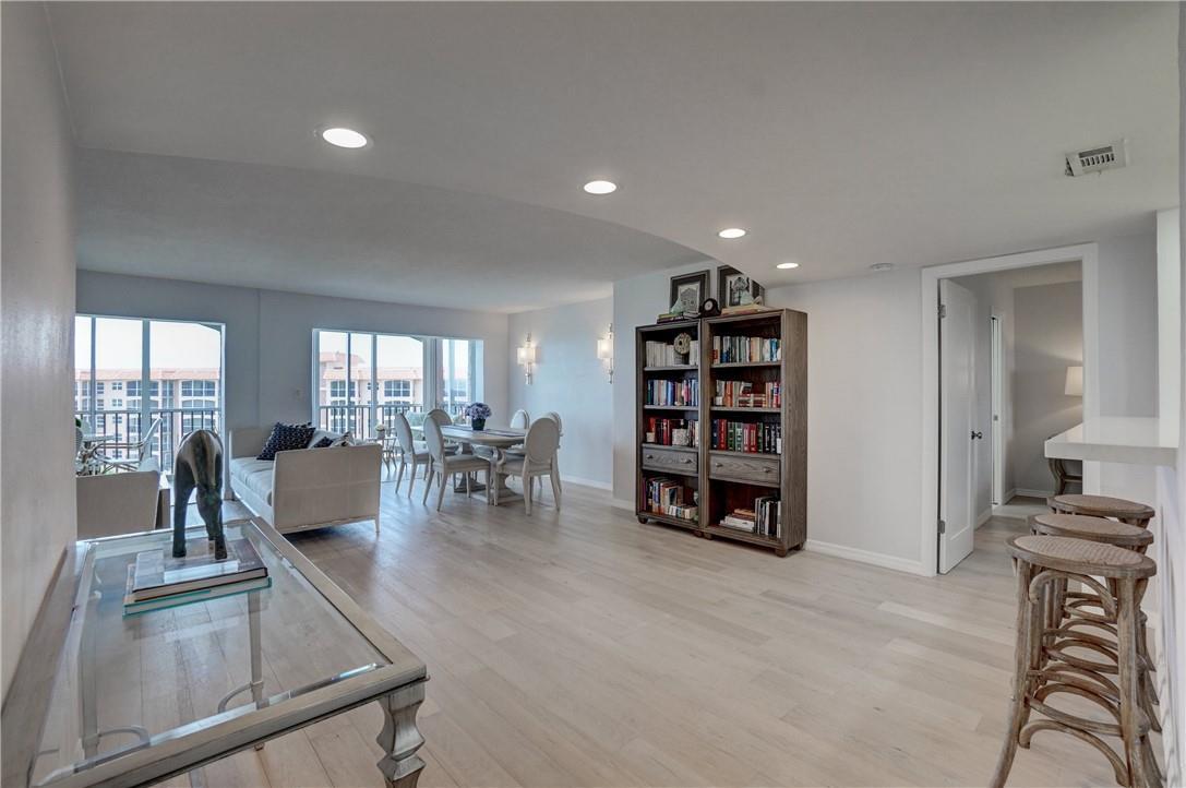 A bright living and dining area with light wood floors, a bookshelf, and balcony access — 2871 N Ocean Boulevard # C519, Boca Raton FL 33431, BOCA RATON, FL