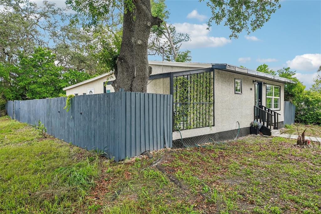 A single-story house with a grey fence and a large tree growing near the porch — 8514 N BRANCH AVENUE, TAMPA, FL