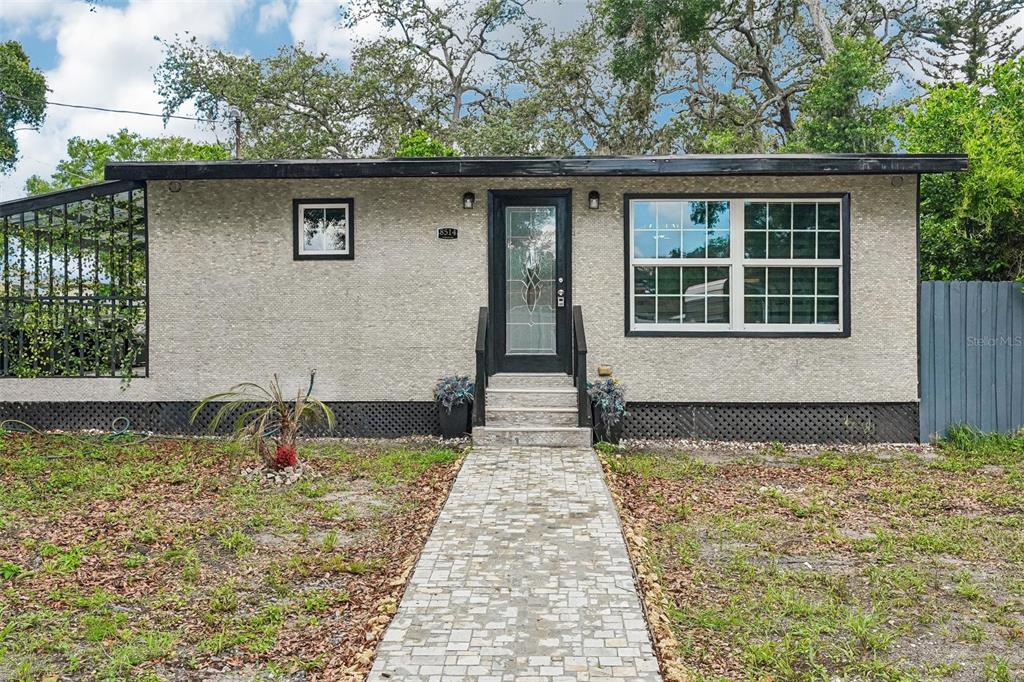 A single-story house with a textured light-colored facade, black trim, and a stone walkway — 8514 N BRANCH AVENUE, TAMPA, FL