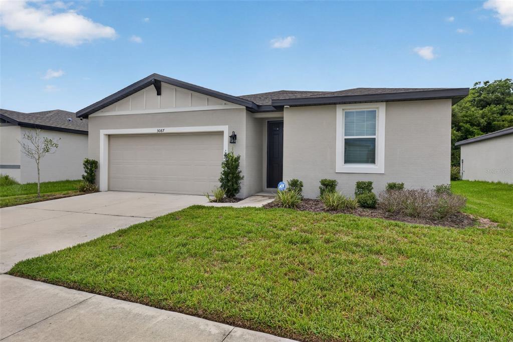 A single-story house with a beige stucco exterior, a two-car garage, and a front lawn — 3087 FORREST PLUM COURT, ZEPHYRHILLS, FL