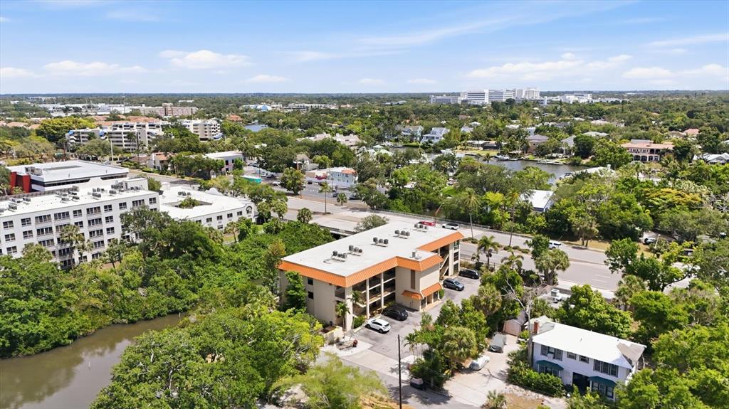 An aerial view shows a multi-story apartment building surrounded by trees and a nearby waterway — 1650 PINE TREE LANE UNIT 103, SARASOTA, FL