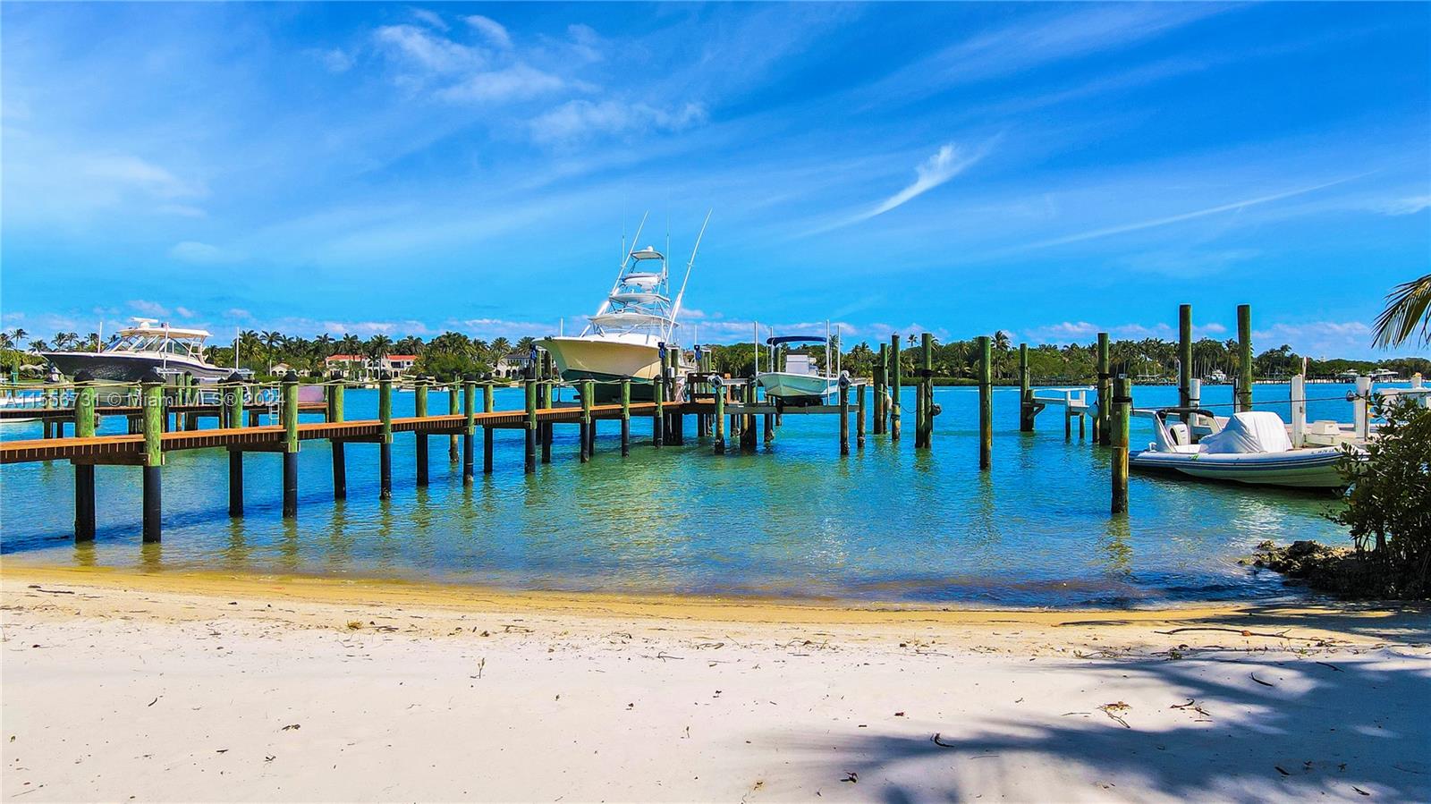 A wooden dock extends into a turquoise bay with several boats moored under a blue sky — 17581 SE Conch Bar Ave, Jupiter FL 33469, JUPITER, FL