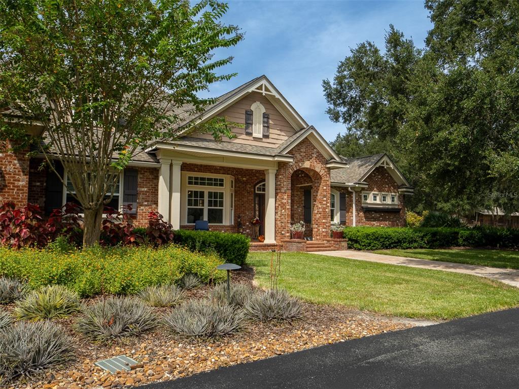 A brick house with a gabled roof, front porch, and landscaped yard under a blue sky — 15122 NW 41ST AVENUE, NEWBERRY, FL