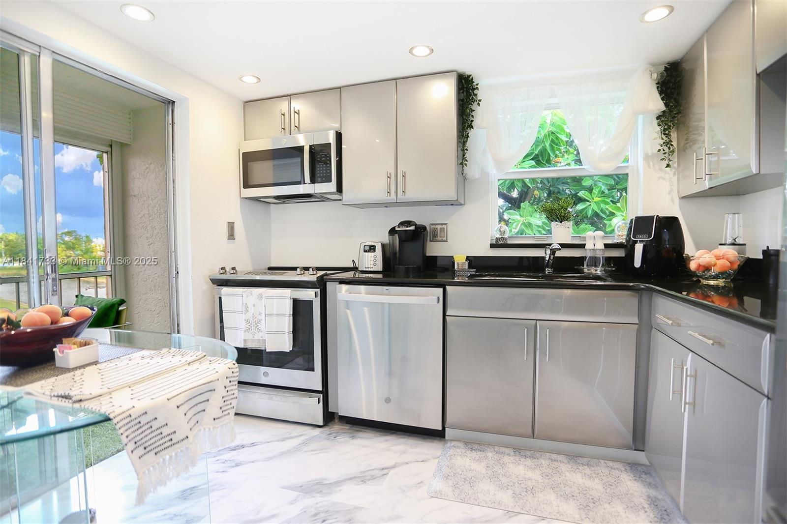 A kitchen features stainless steel appliances, grey cabinets, black countertops, and marble-look flooring — 6570 Royal Palm Blvd # 301J, Margate FL 33063, MARGATE, FL