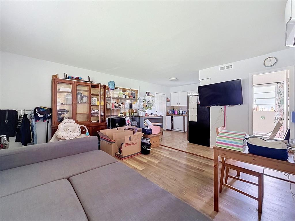 A living room with wood-look flooring flows into a kitchen with white cabinets and appliances — 7995 53RD WAY N, PINELLAS PARK, FL