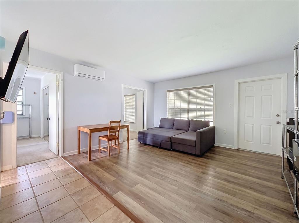 A living room with wood-look flooring, a grey sectional sofa, a desk, and a wall-mounted AC — 7995 53RD WAY N, PINELLAS PARK, FL