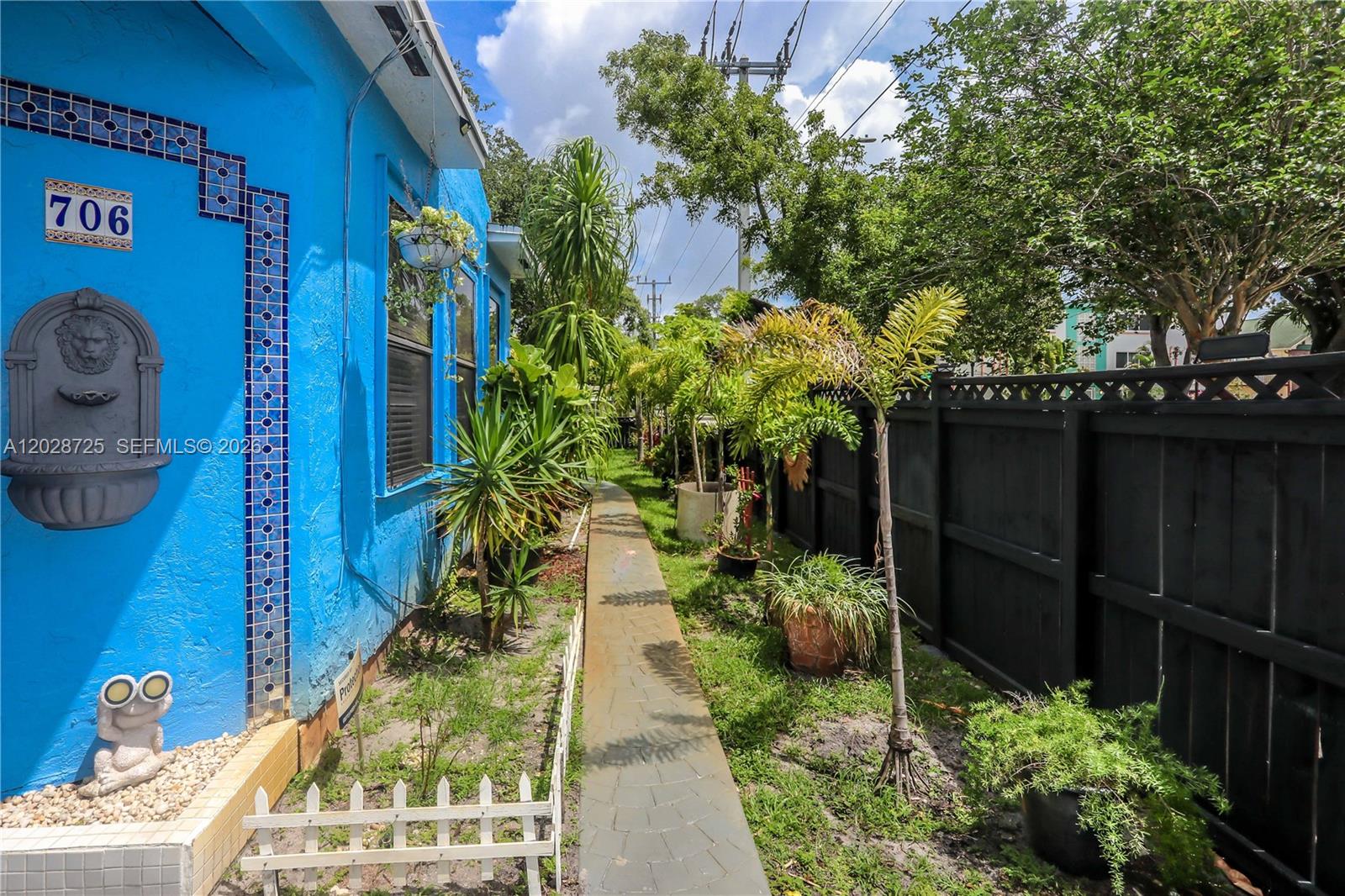 A narrow stone walkway runs between a bright blue house and a black wooden fence — 706 S 19th Ave, Hollywood FL 33020, HOLLYWOOD, FL