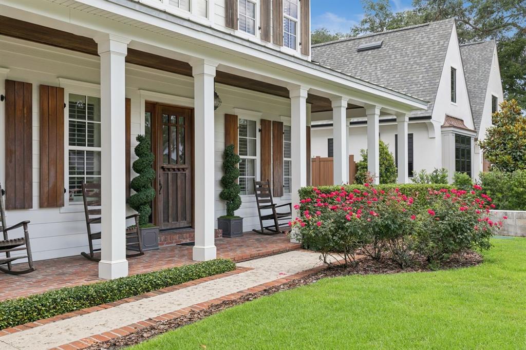 A white farmhouse-style home features a brick porch, wooden shutters, and a landscaped front yard — 2240 VENETIAN WAY, WINTER PARK, FL