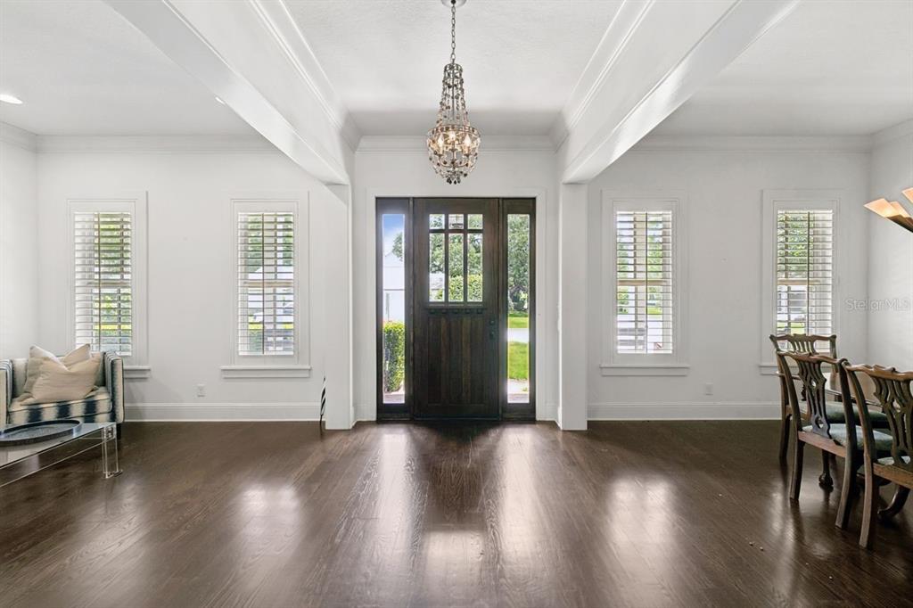 A bright foyer features dark hardwood floors, a crystal chandelier, and a wooden front door — 2240 VENETIAN WAY, WINTER PARK, FL
