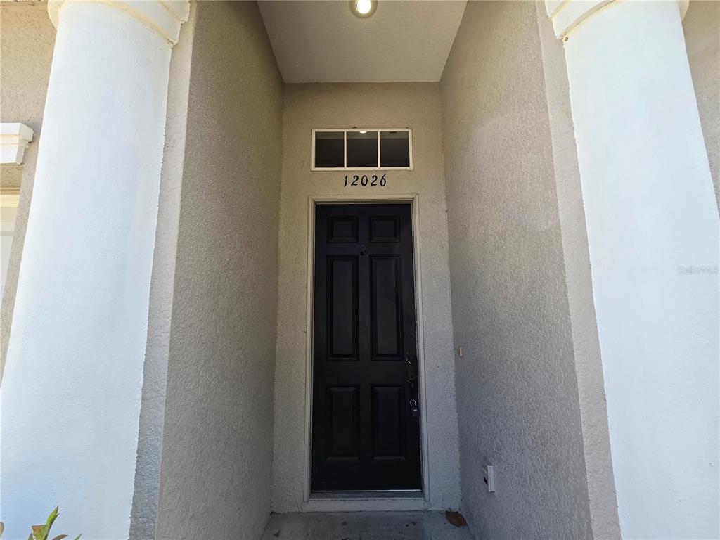A black front door with a transom window is set within a recessed entryway — 12026 TASHA COURT, NEW PORT RICHEY, FL