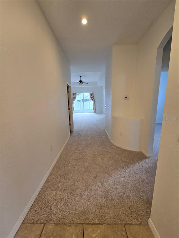 A carpeted hallway leads toward a living area with a ceiling fan and sliding doors — 12026 TASHA COURT, NEW PORT RICHEY, FL