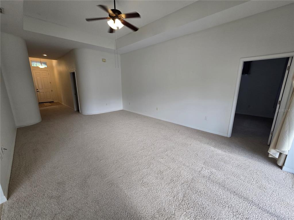 A spacious living room features beige carpeting, white walls, a tray ceiling, and a ceiling fan — 12026 TASHA COURT, NEW PORT RICHEY, FL