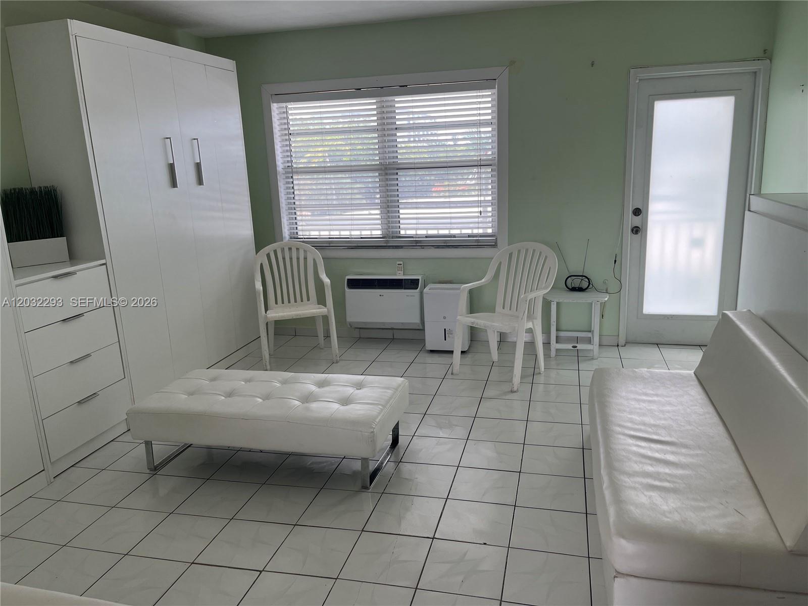 A room with white tile floors, a white wardrobe, two plastic chairs, and a sofa — 851 Meridian Ave # 44, Miami Beach FL 33139, MIAMI BEACH, FL