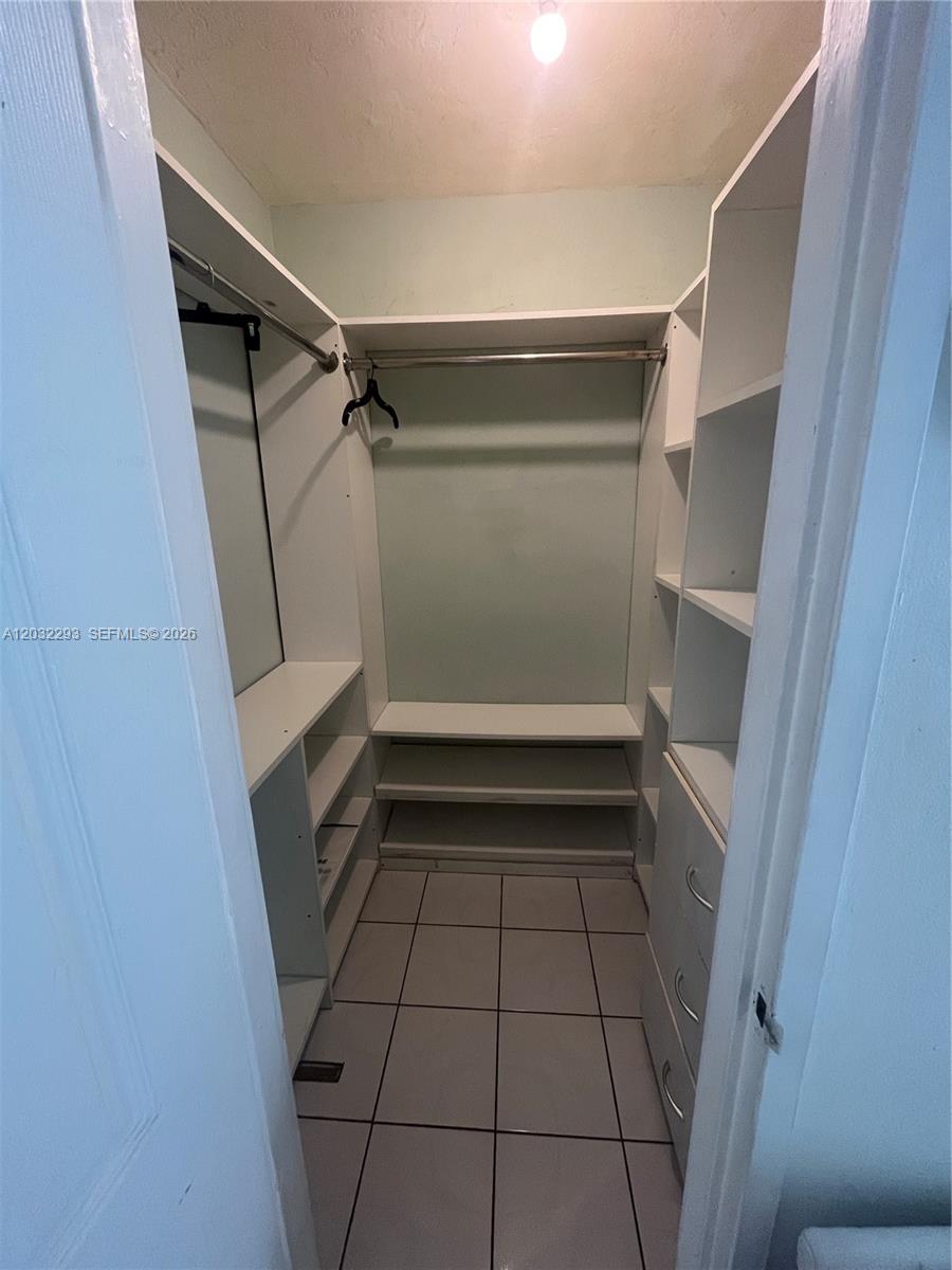 A walk-in closet features white built-in shelving, hanging rods, drawers, and tiled flooring — 851 Meridian Ave # 44, Miami Beach FL 33139, MIAMI BEACH, FL