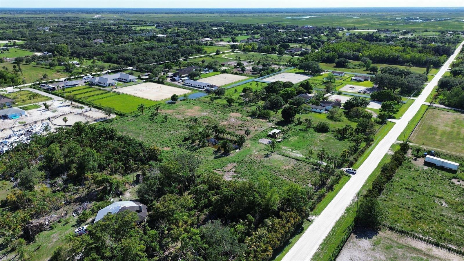 An aerial view shows a rural property with multiple buildings, equestrian arenas, and surrounding greenery — 16290 Rustic Road, Wellington FL 33470, WELLINGTON, FL