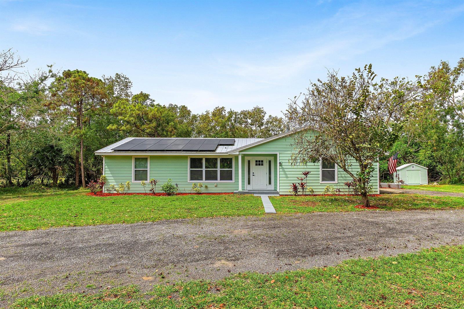 A light green single-story house with solar panels on the roof and a white front door — 4397 Avocado Boulevard, West Palm Beach FL 33411, WEST PALM BEACH, FL