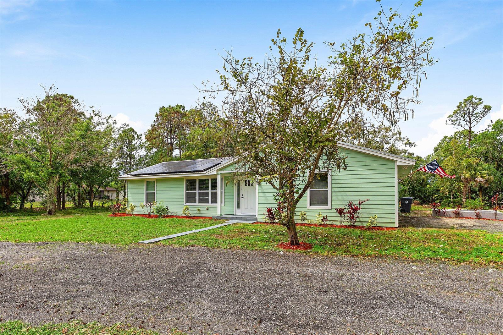 A light green, single-story house with solar panels on the roof and a gravel driveway — 4397 Avocado Boulevard, West Palm Beach FL 33411, WEST PALM BEACH, FL