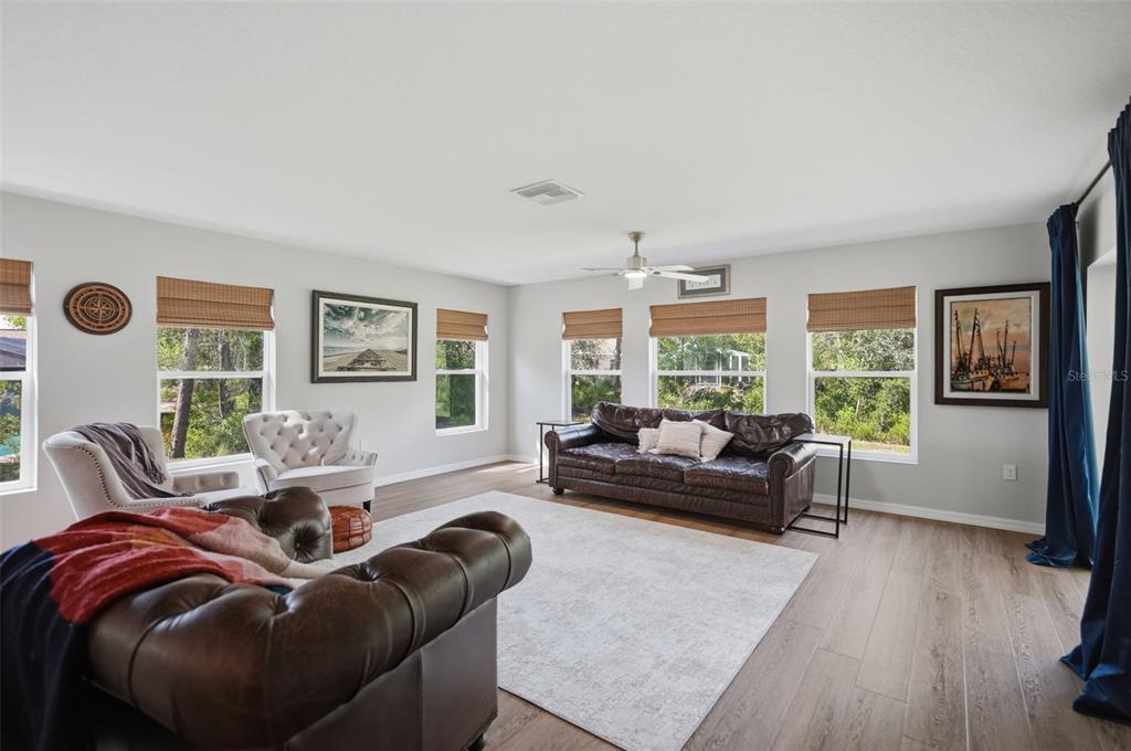 A living room features leather sofas, a light-colored area rug, and multiple windows with shades — 8477 BEACHWOOD COURT, SPRING HILL, FL