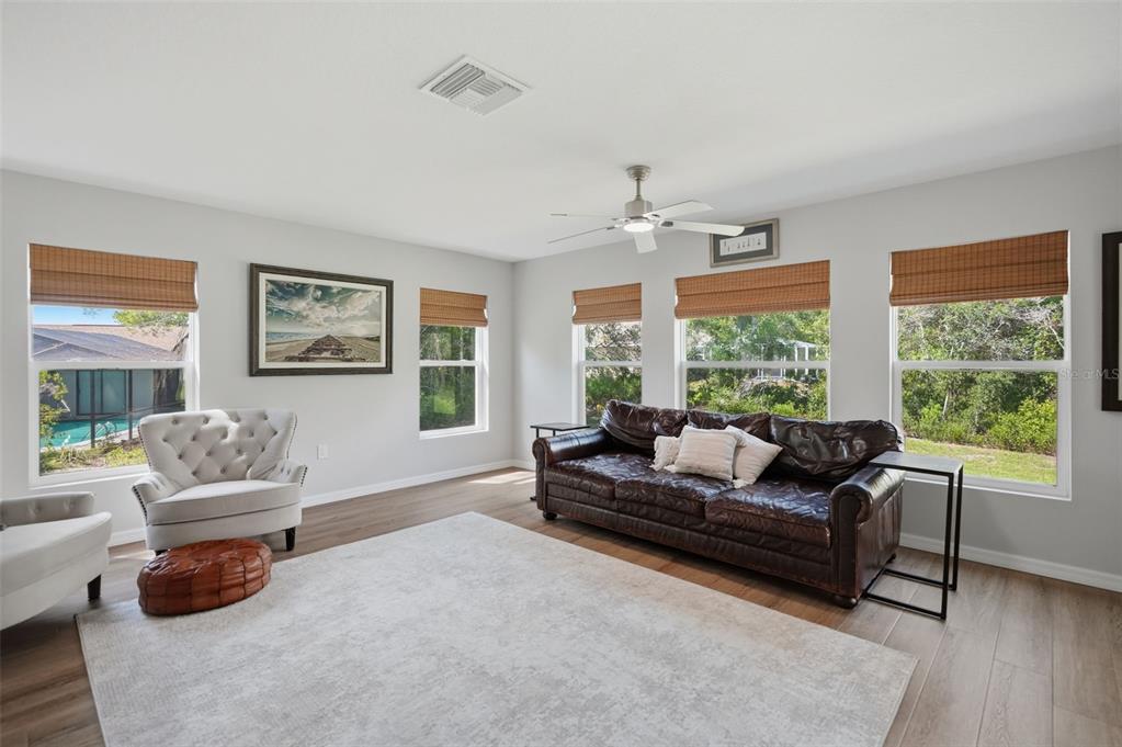 A living room features light wood floors, a leather sofa, armchairs, and several large windows — 8477 BEACHWOOD COURT, SPRING HILL, FL