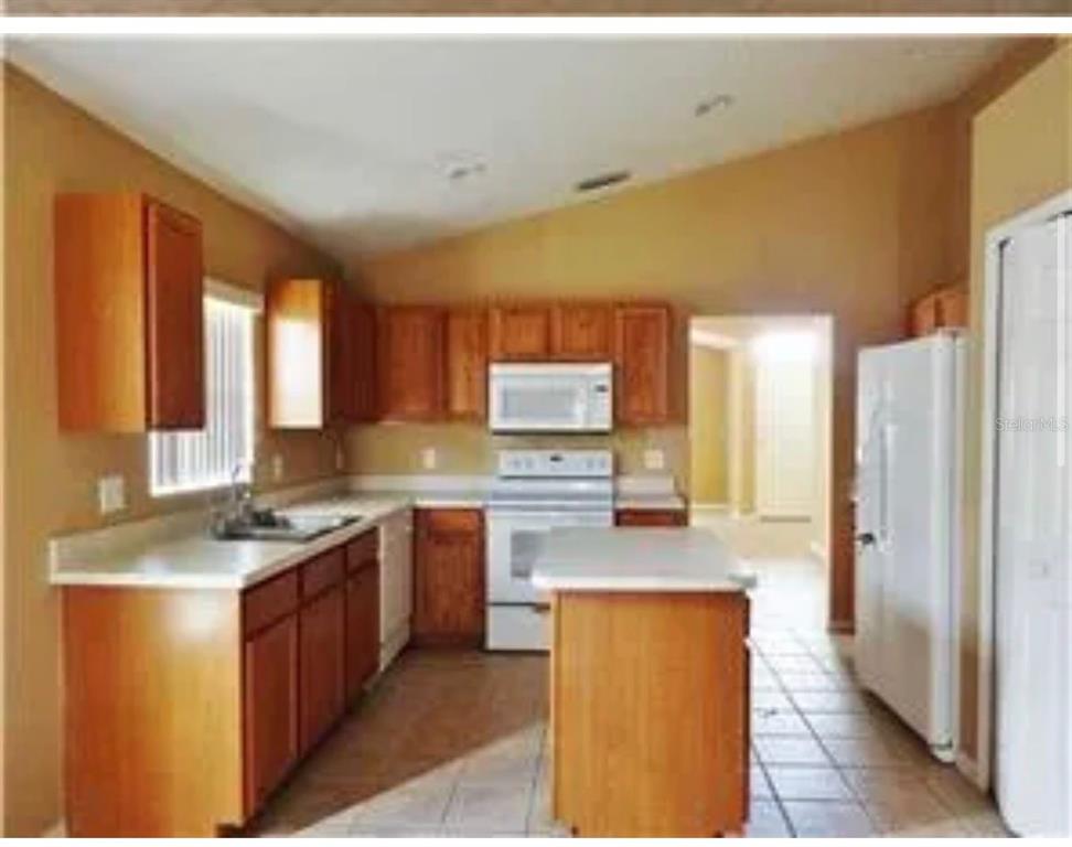 A kitchen with wood cabinets, white appliances, a center island, and tiled flooring — 855 BRAYTON LANE, DAVENPORT, FL