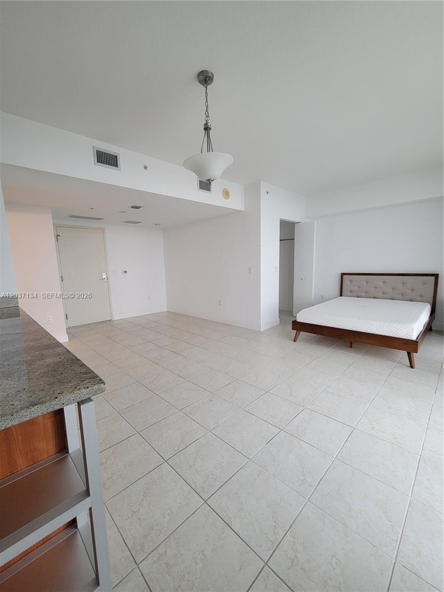 An open-concept studio apartment features tile flooring, a kitchen counter, and a bed frame — 185 SW 7th St # 3500, Miami FL 33130, MIAMI, FL