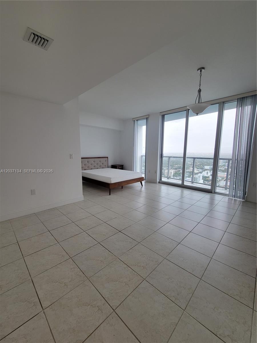 A bedroom features light tile flooring, a bed, and floor-to-ceiling windows with a city view — 185 SW 7th St # 3500, Miami FL 33130, MIAMI, FL