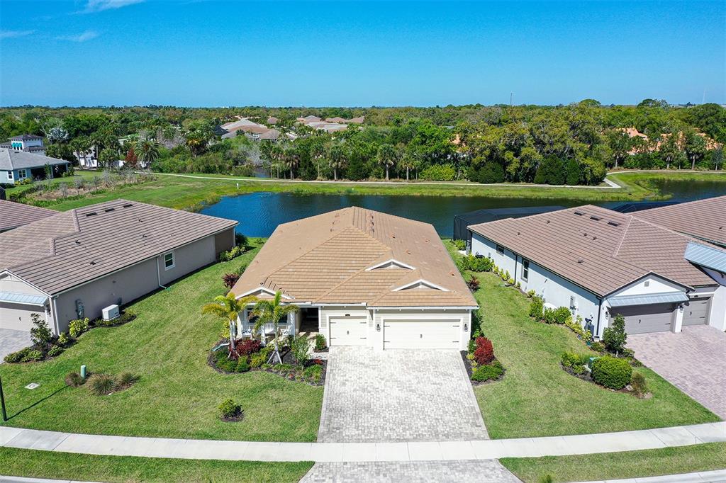 An aerial view shows a single-story house with a tiled roof, driveway, and backyard pond — 5521 BLUE WATER BOULEVARD, SARASOTA, FL