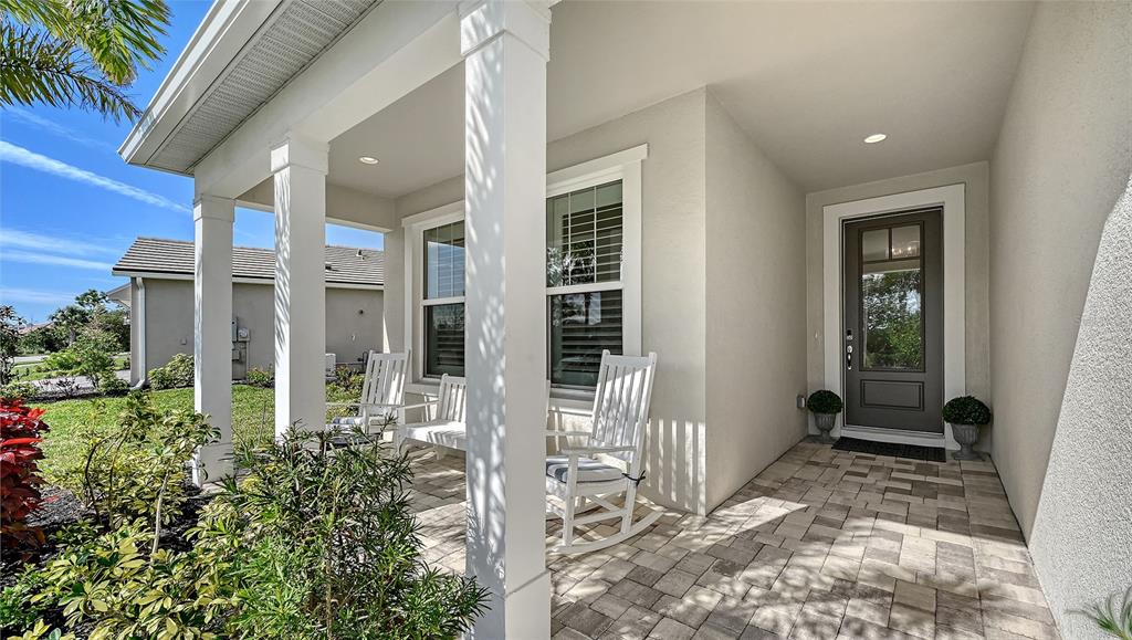 A covered front porch features white columns, rocking chairs, and a dark-framed glass door — 5521 BLUE WATER BOULEVARD, SARASOTA, FL
